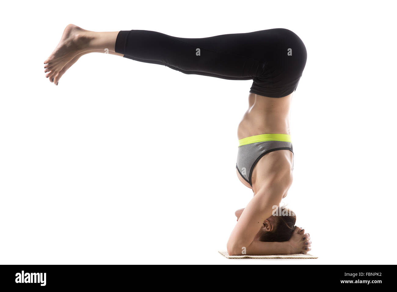 Sporty fit beautiful young brunette woman in sportswear bra and black pants working out, doing Headstand Half Fold pose Stock Photo