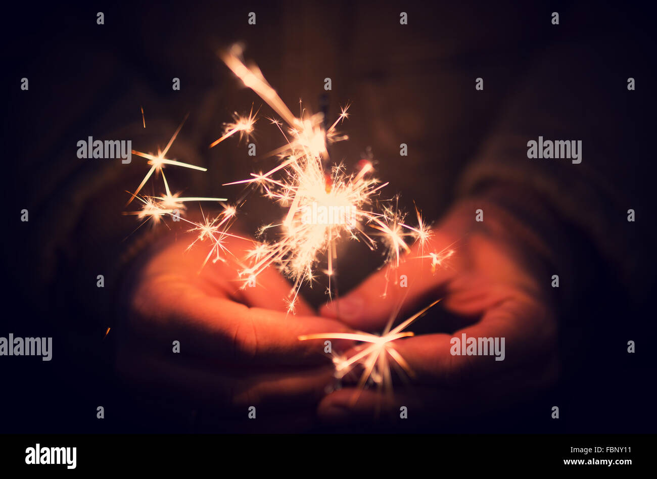 Man holding bright festive Christmas sparkler in hand, tinted ph Stock Photo