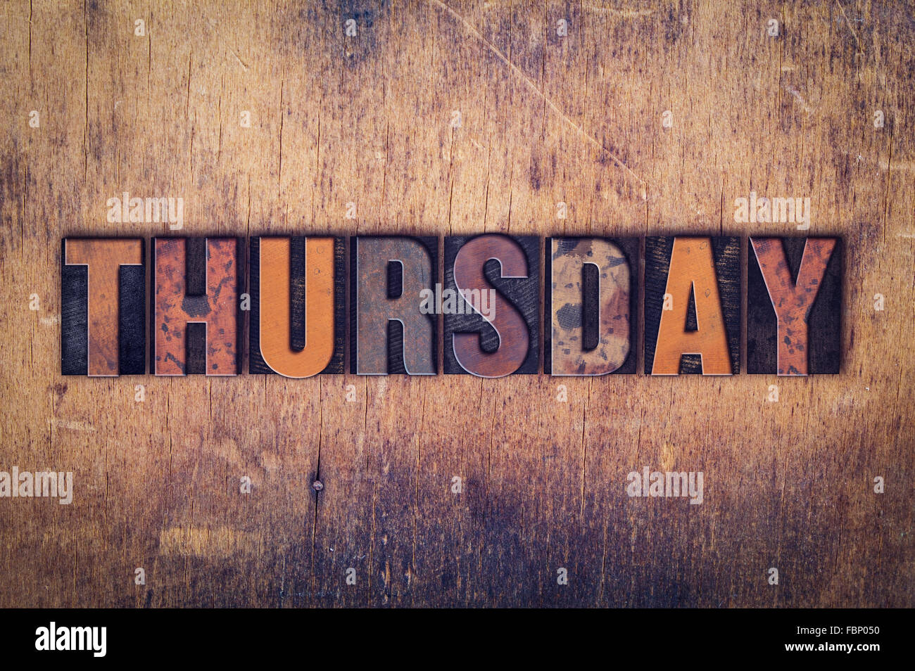 The word "Thursday" written in dirty vintage letterpress type on a aged wooden background. Stock Photo