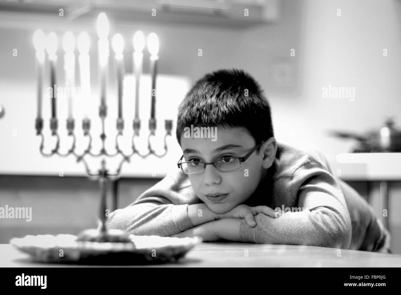 Cute Boy Looking At Lit Candles While Sitting On Table At Home Stock Photo