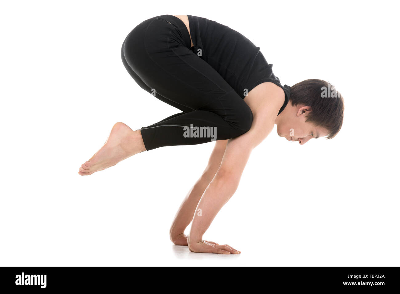 Sporty young man working out, doing handstand yoga asana, Crane (Crow) Pose, Bakasana for shoulders, upper back, arms and wrists Stock Photo