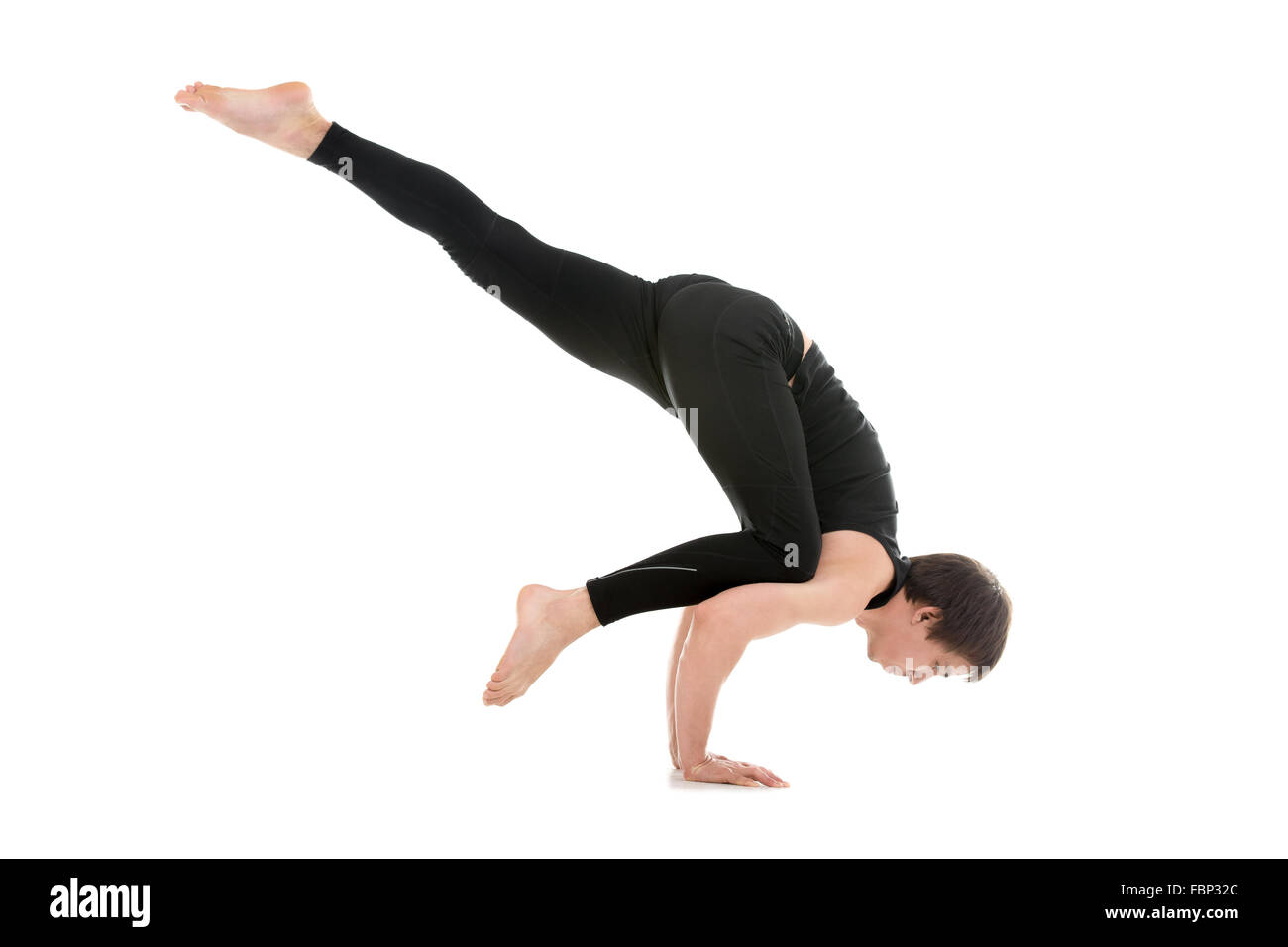 Sporty young man working out, doing arm balancing handstand yoga asana, One Legged Crane Pose, Half Crow Pose, Eka Pada Bakasana Stock Photo