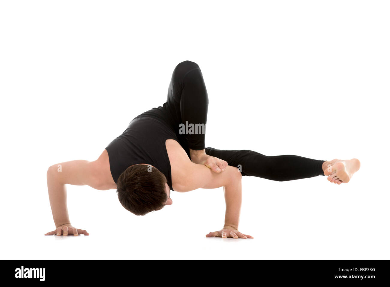 Sporty young man doing Arm balance exercise for strength, yoga, pilates training, asana Parivritta Eka Pada Koundinyasana Stock Photo