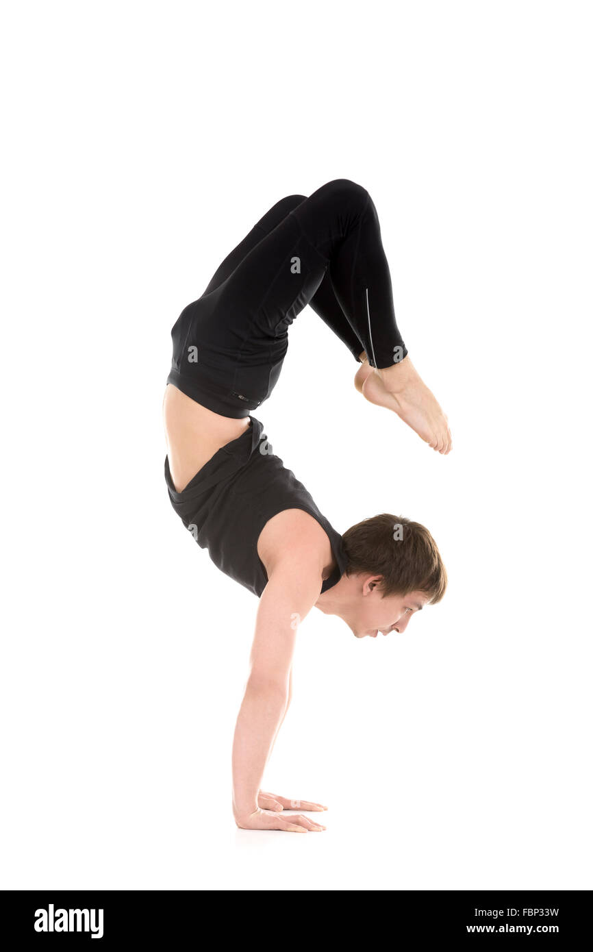 Profile of sporty yogi young man working out, yoga, pilates, fitness training, doing handstand, asana Vrischikasana 2, Scorpion Stock Photo