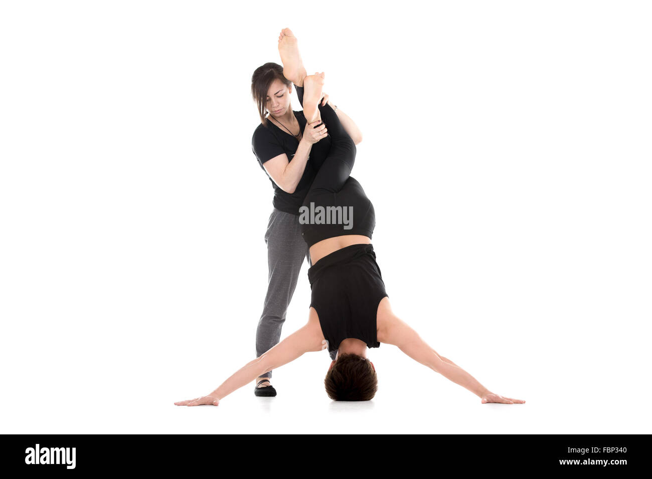 Two sporty people working out, practicing yoga, pilates, fitness, young woman coach assisting male student in Iron Cross Stock Photo