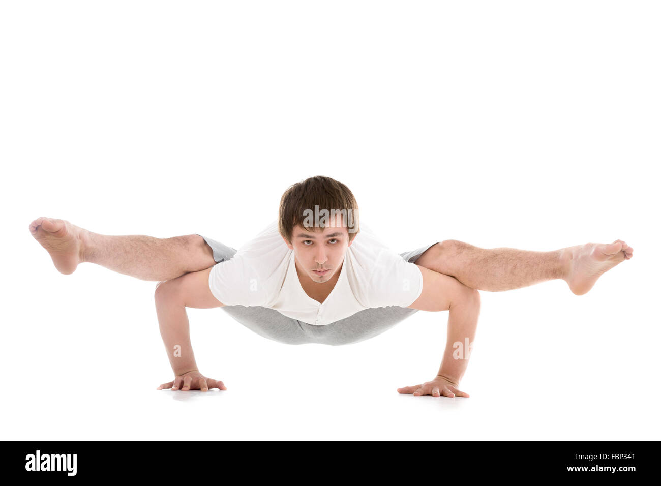 Sporty young man working out, yoga, pilates, fitness training, arm balance Firefly posture, asana Tittibhasana, Insect Pose Stock Photo