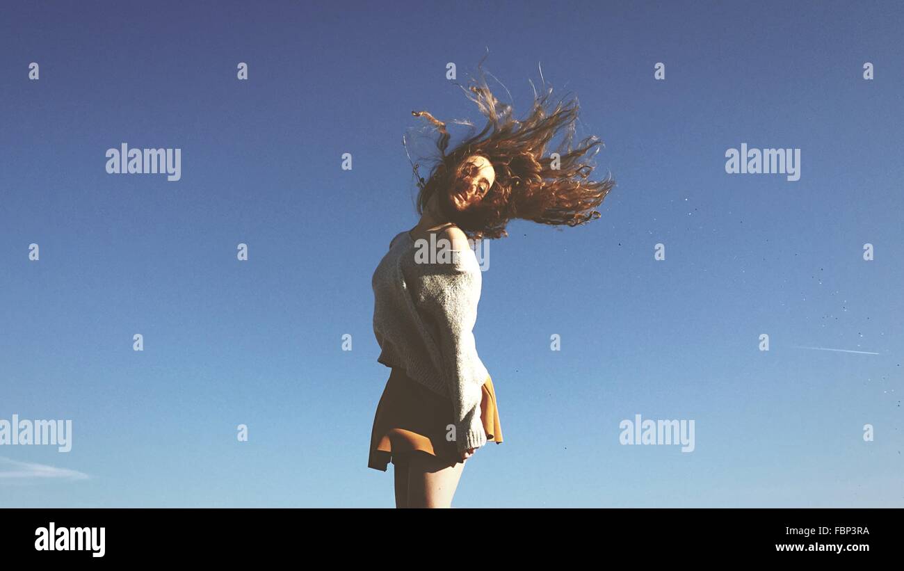 Young Woman Tossing Hair Against Clear Blue Sky Stock Photo