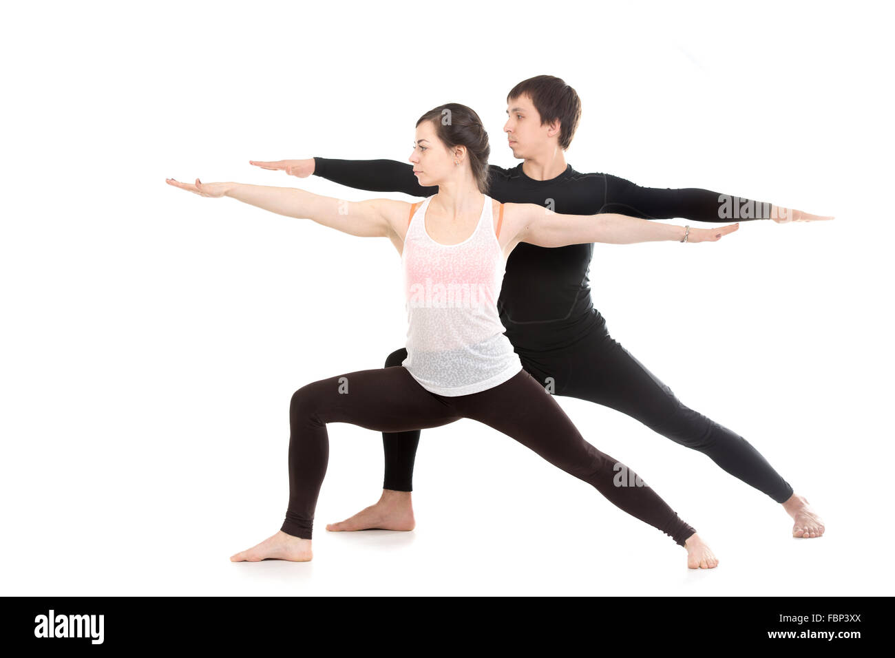 Two sporty people practice yoga with partner, doing lunge exercise, Warrior II posture, Virabhadrasana 2, side view Stock Photo