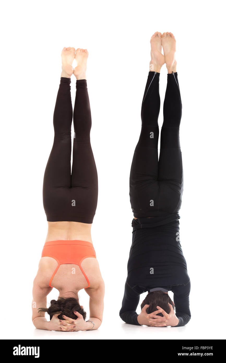 Two sporty people practice yoga in pair, acroyoga, fit couple doing supported headstand yoga asana, salamba sirsasana Stock Photo