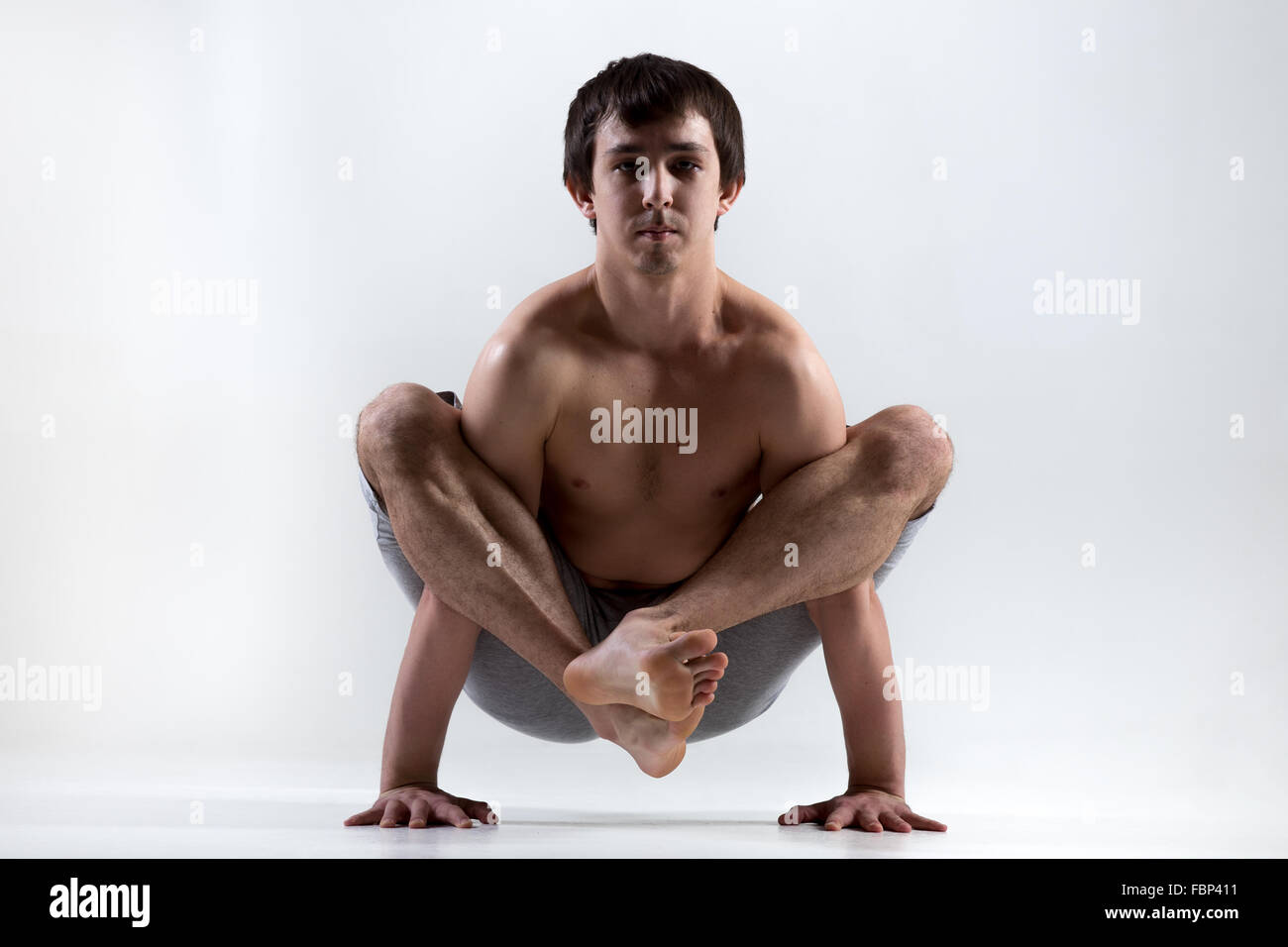 Sporty young man working out, yoga, pilates, fitness training, Bhujapidasana, Shoulder-Pressing Pose, handstand Stock Photo