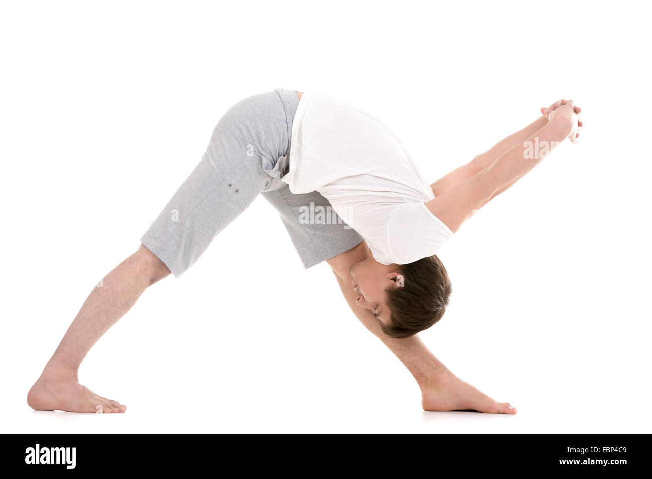 Sporty young man working out, yoga, pilates, fitness training, doing Pyramid Pose, Intense Side Stretch Posture, Parsvottanasana Stock Photo