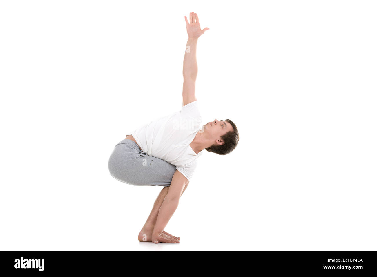 Sporty young man working out, standing in variation of Revolved Chair twist Pose, Parivrtta utkatasana with extended arms Stock Photo