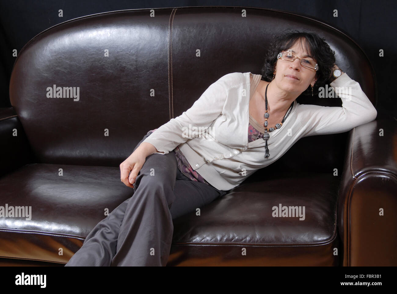 a pretty mature woman sitting on a sofa Stock Photo - Alamy