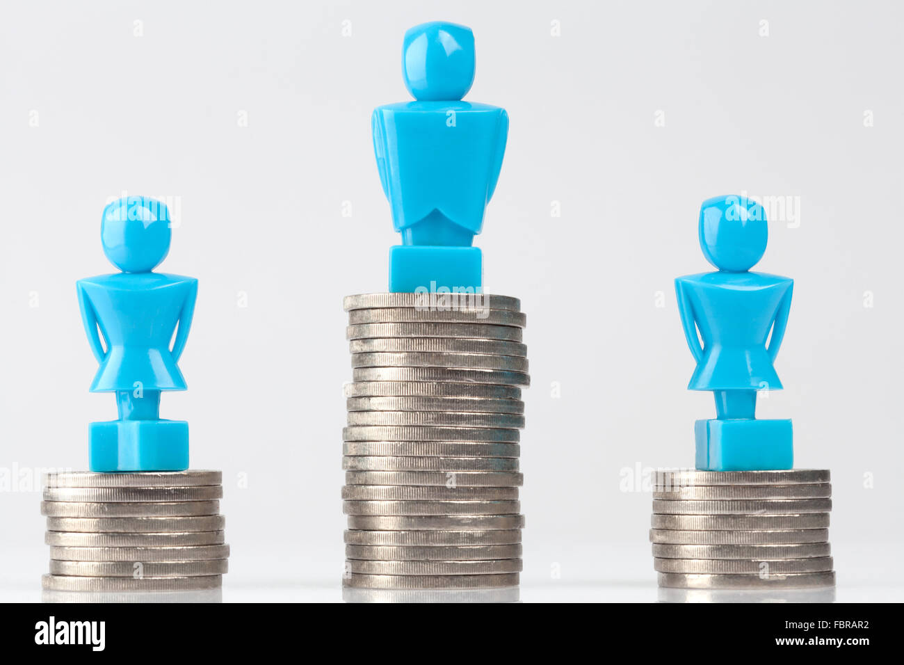One male and two female figurines standing on piles of coins. Hero look. Income inequality concept. Stock Photo