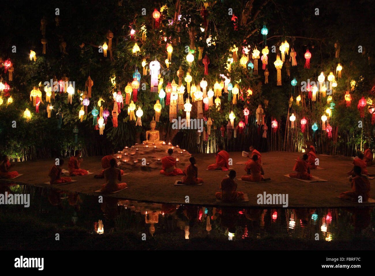 Chiang Mai, Thailand, 2016. Monks in saffron robes sitting under tree lit with hundreds of lanterns in prayer. Stock Photo