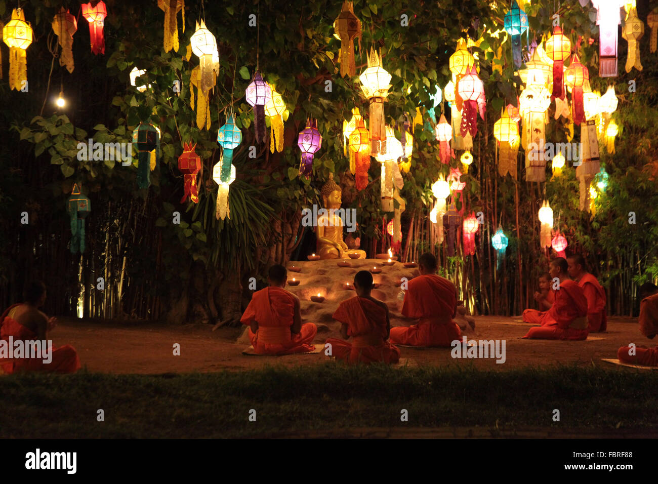 Chiang Mai, Thailand, 2016. Monks in saffron robes sitting under tree lit with hundreds of lanterns in prayer. Stock Photo