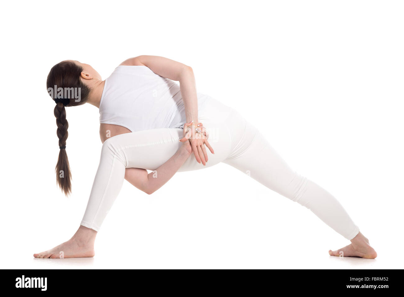Sporty attractive young woman in white sportswear doing lunge exercise, variation of utthita parshvakonasana with hands behind Stock Photo