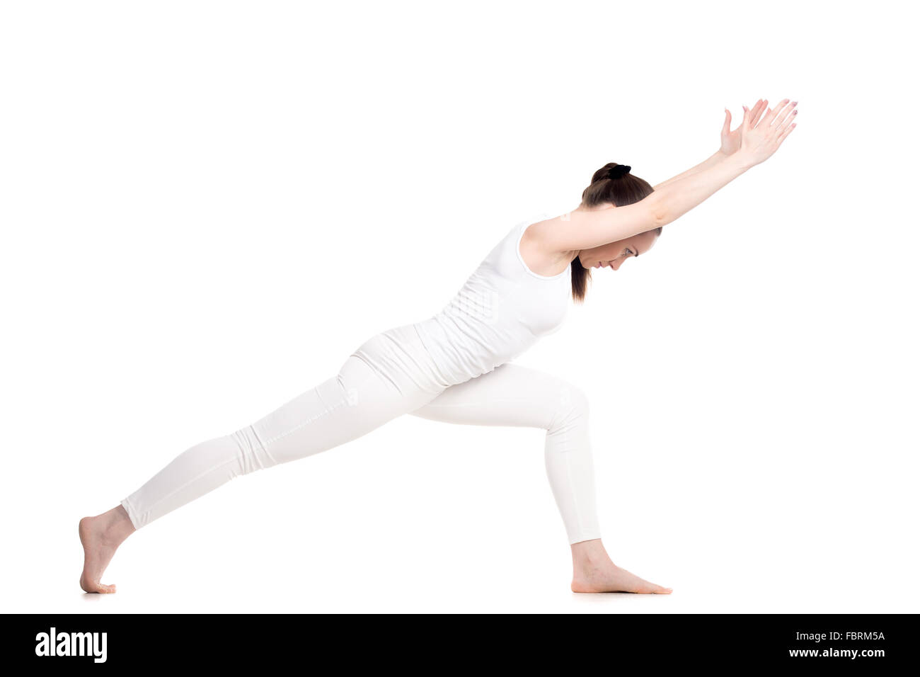 Sporty beautiful young woman in white sportswear doing lunge exercise, standing in Warrior I posture variation, Virabhadrasana 1 Stock Photo