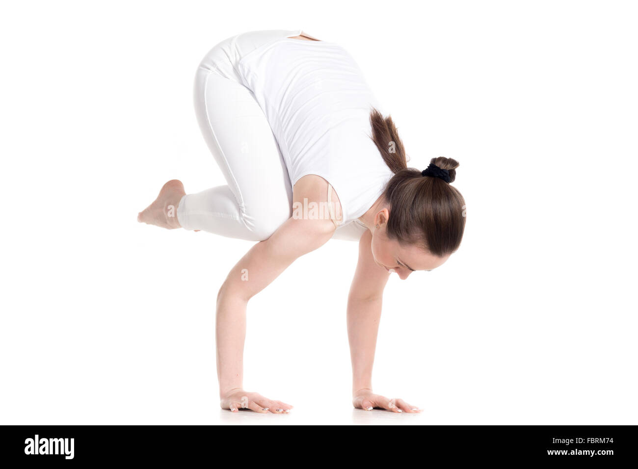 Sporty beautiful young woman in white sportswear doing handstand yoga asana, exercise for arm strength, Crane (Crow) Pose Stock Photo