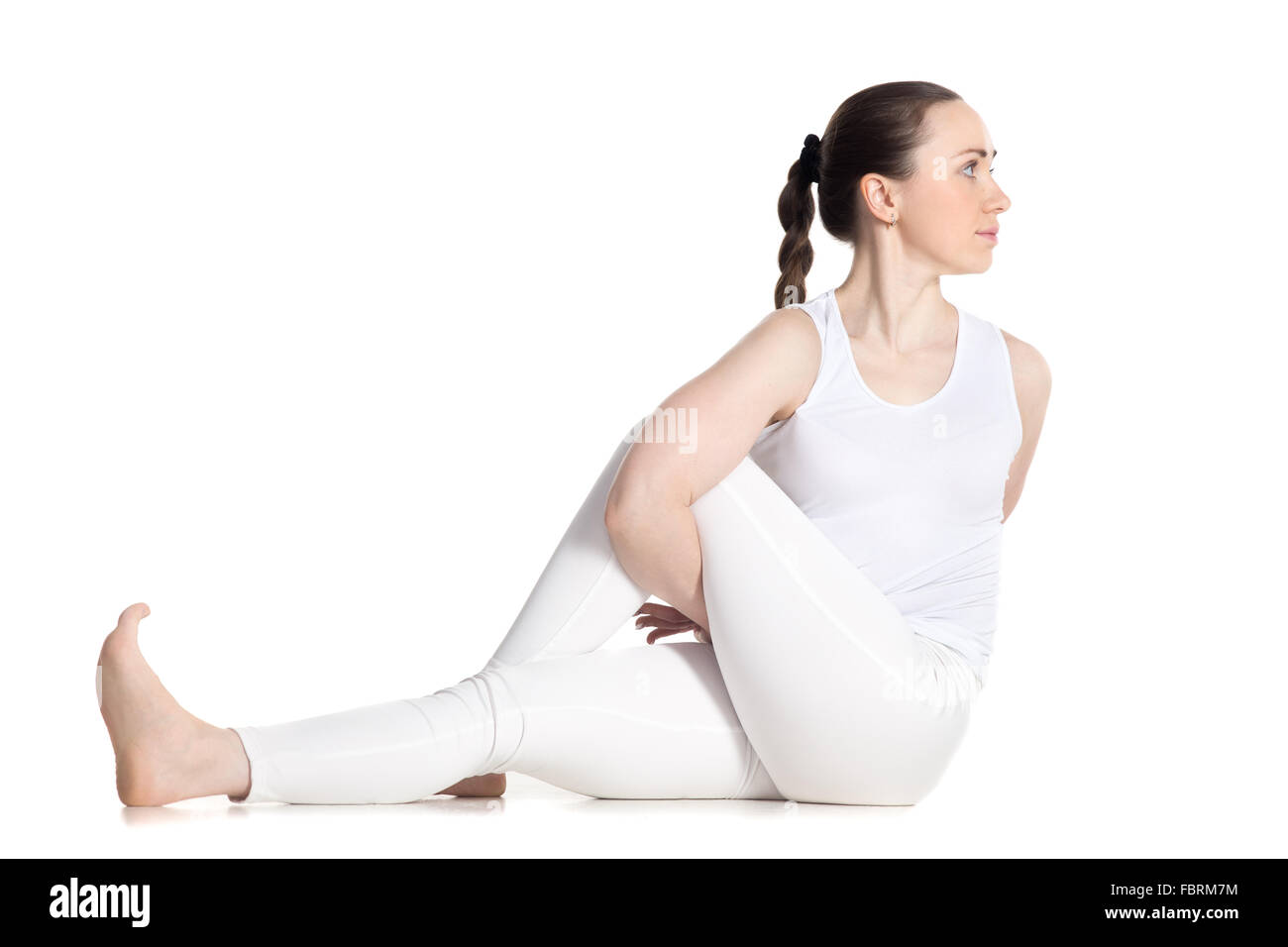 Sporty beautiful young woman in white sportswear practicing yoga, sitting in variation of Half lord of the fishes pose, Ardha Stock Photo