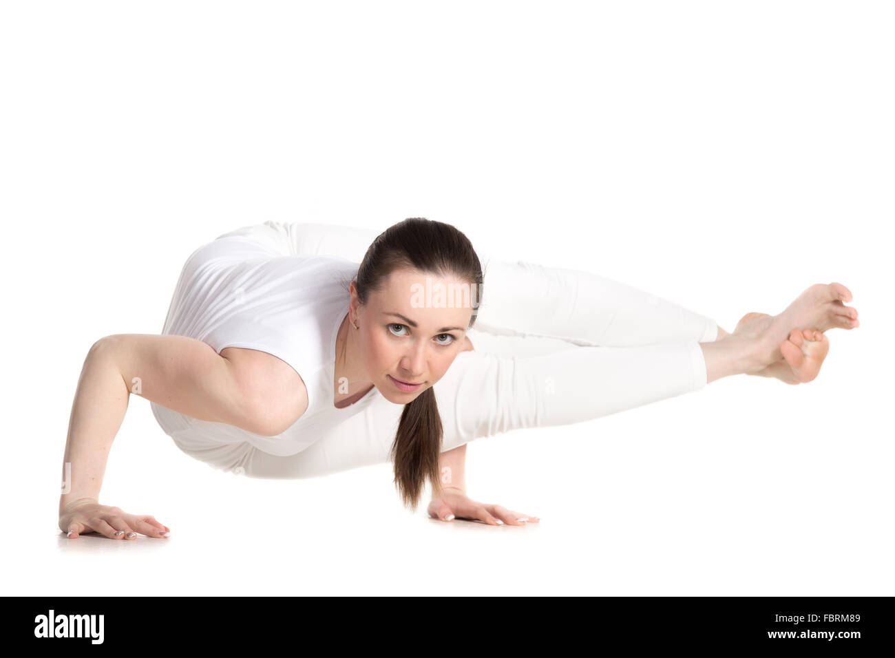 Sporty beautiful young woman in white sportswear doing arm stand Astavakrasana, asymmetrical arm balance Eight-Angle Pose Stock Photo