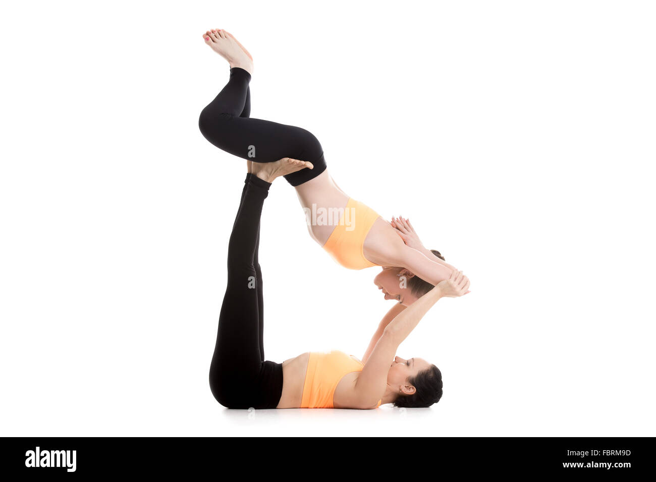 Two sporty girls on white background doing acroyoga, yoga with partner, Reclining Bound Angle Pose, Supta Baddha Konasana Stock Photo