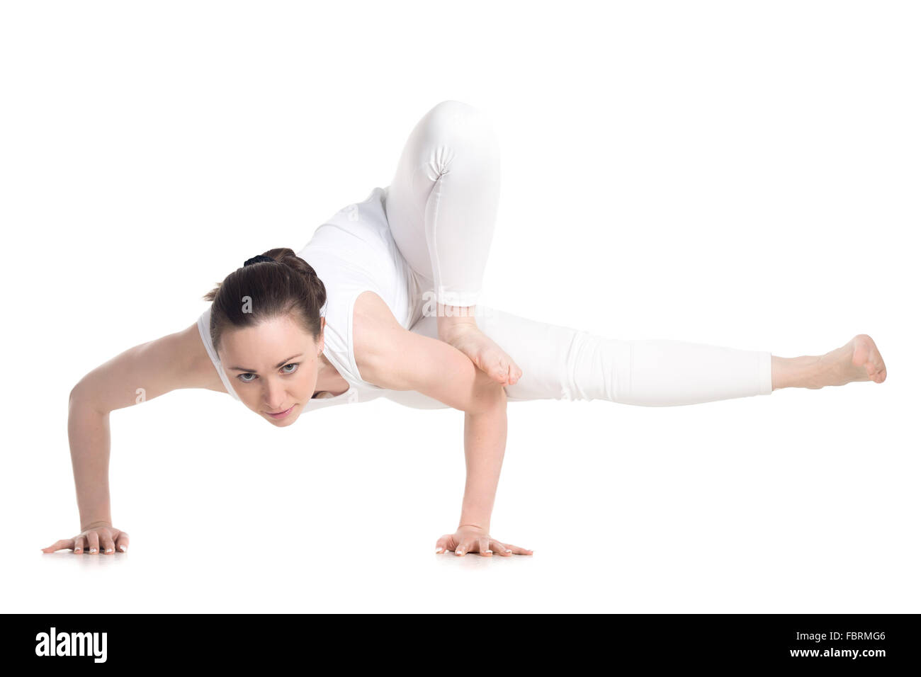 Sporty beautiful young woman in white sportswear standing in Dragonfly yoga Pose, maksikanagasana, Parivrtta Eka Pada Danda Stock Photo