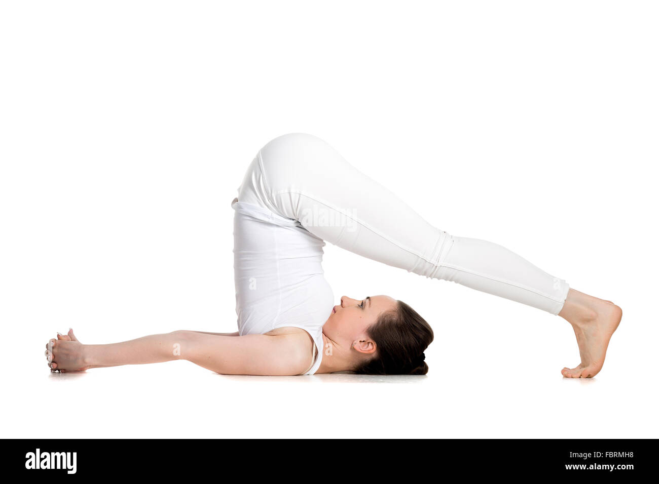 Sporty beautiful young woman doing halasana, plough pose (yin yoga snail posture), studio full length shot on white background Stock Photo