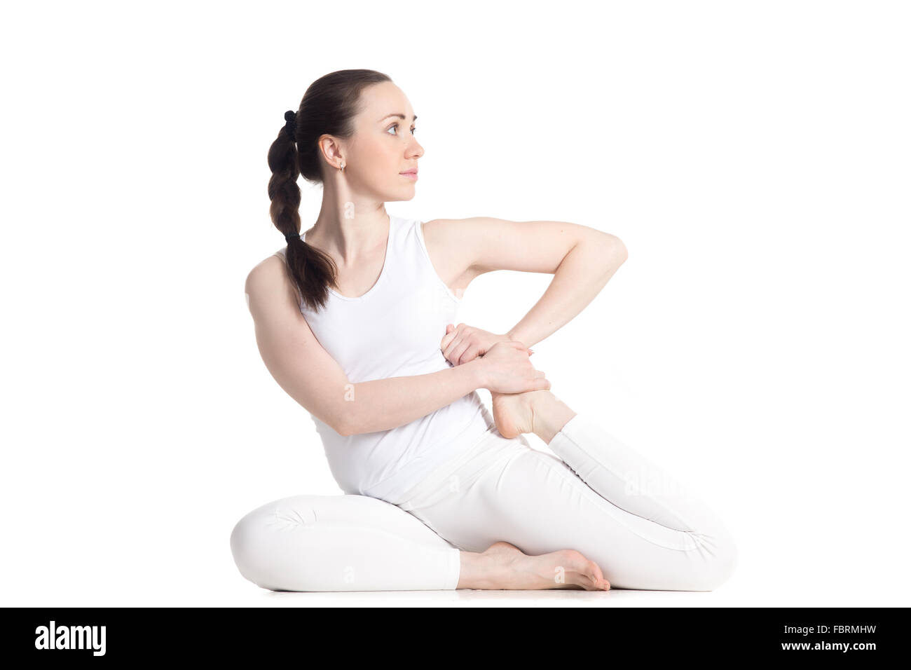 Sporty attractive young woman in white sportswear sitting in variation of pose Dedicated to the Sage Vamadeva, Vamadevasana Stock Photo