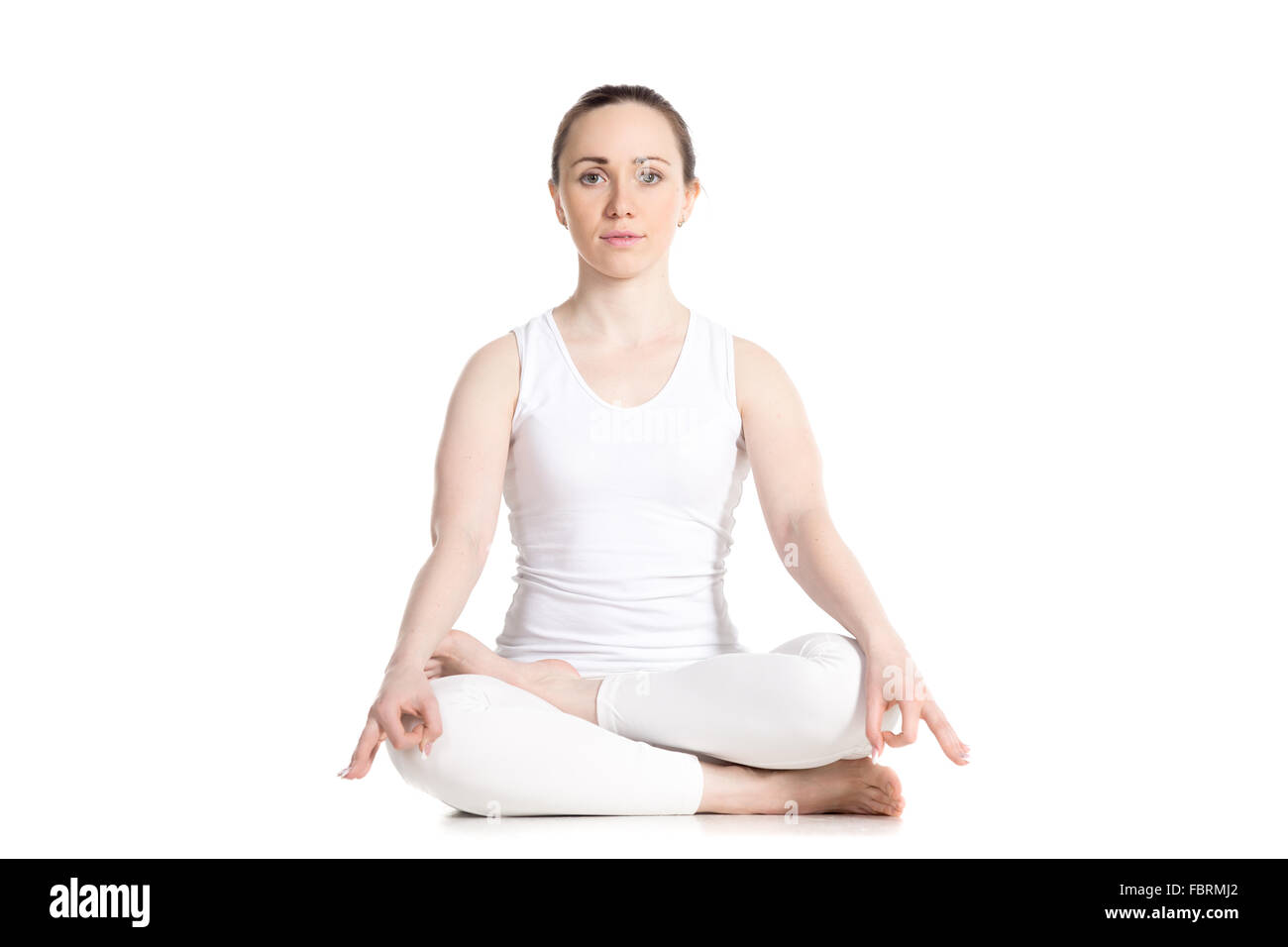 Sporty attractive young woman in white sportswear sitting in Ardha Padmasana, half lotus posture, studio full length front view Stock Photo