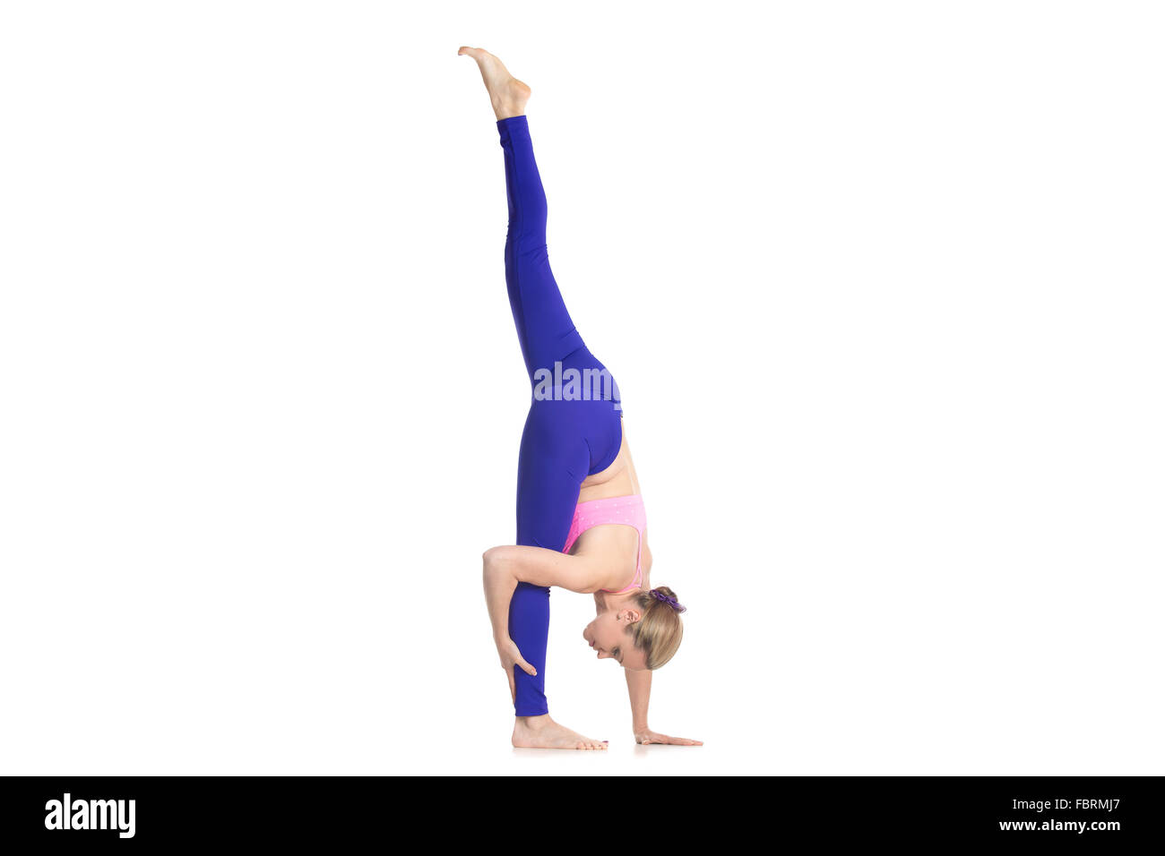 Sporty beautiful young blond woman in purple leggings doing Standing Split yoga pose, Urdhva Prasarita Eka Padasana, studio Stock Photo