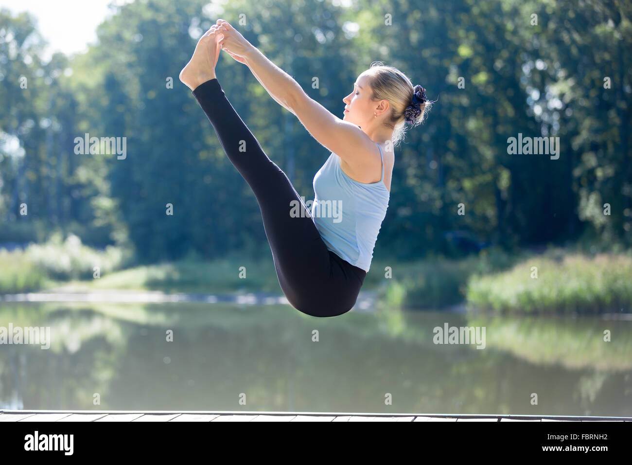 Serene young sporty beautiful woman floating in midair during yoga practice, levitating above ground, doing Both Big Toe posture Stock Photo