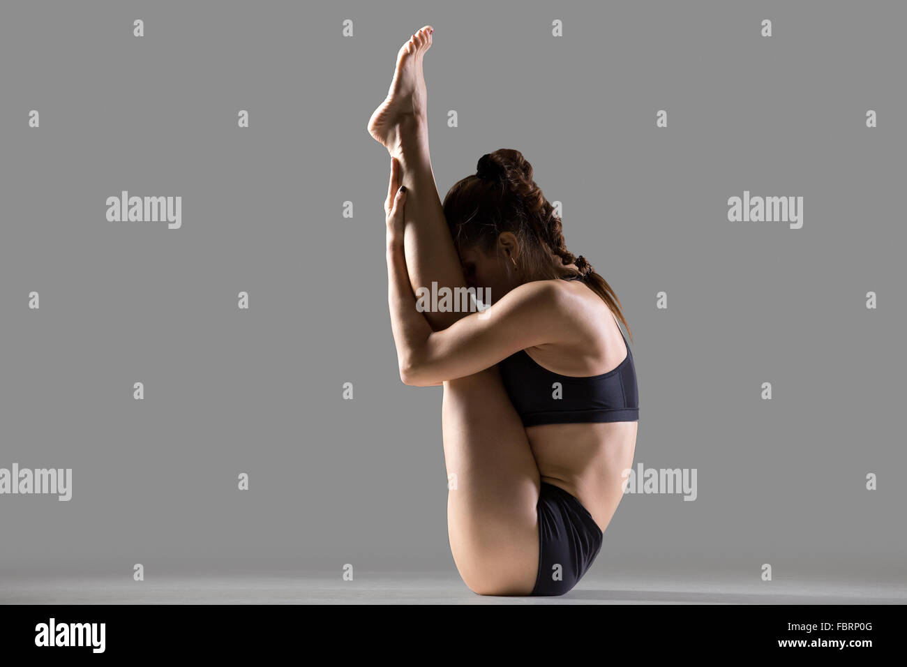 Portrait of beautiful young fit woman in sportswear doing sport exercise, sitting in upward facing forward bend posture Stock Photo
