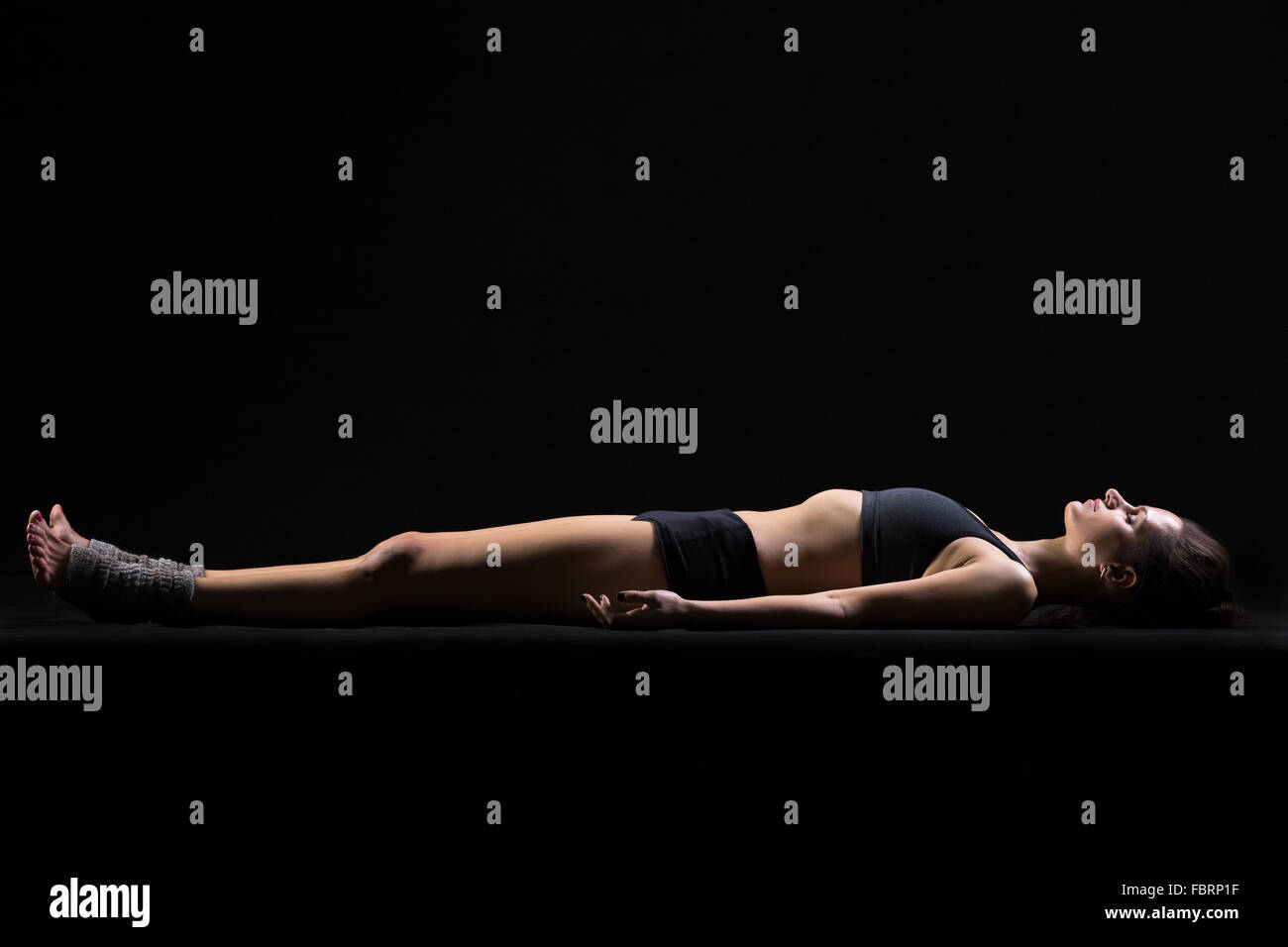 Beautiful cool young fit woman in sportswear lying in Shavasana (Savasana, Corpse or Dead Body Posture), resting after practice Stock Photo