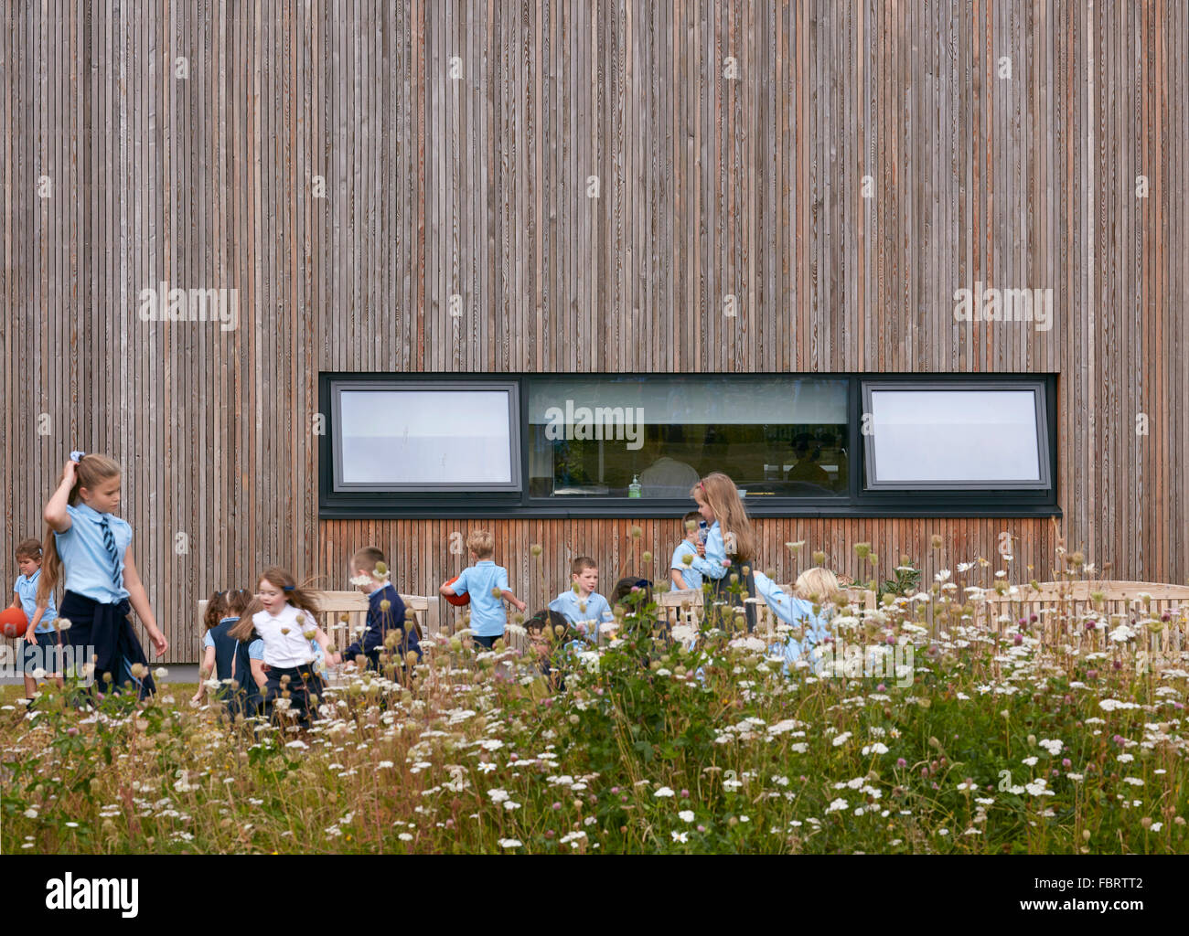 Schoolchildren at play in front of larch clad facade. Lairdsland Primary School, Kirkintilloch, United Kingdom. Architect: Walte Stock Photo