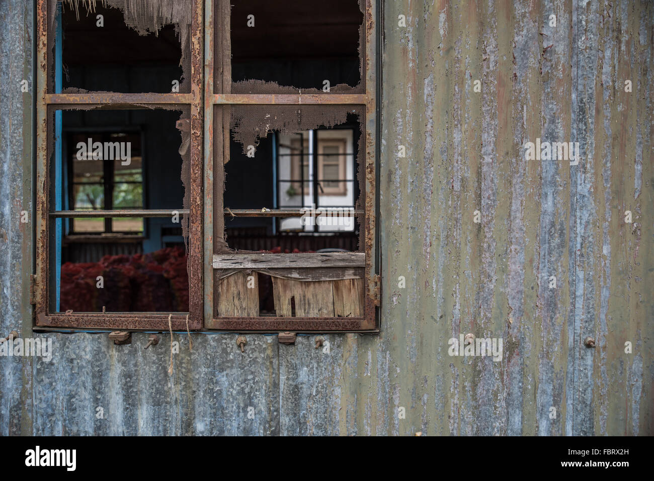 Rusty tarnished corrugated metal wall featuring a rusted window frame