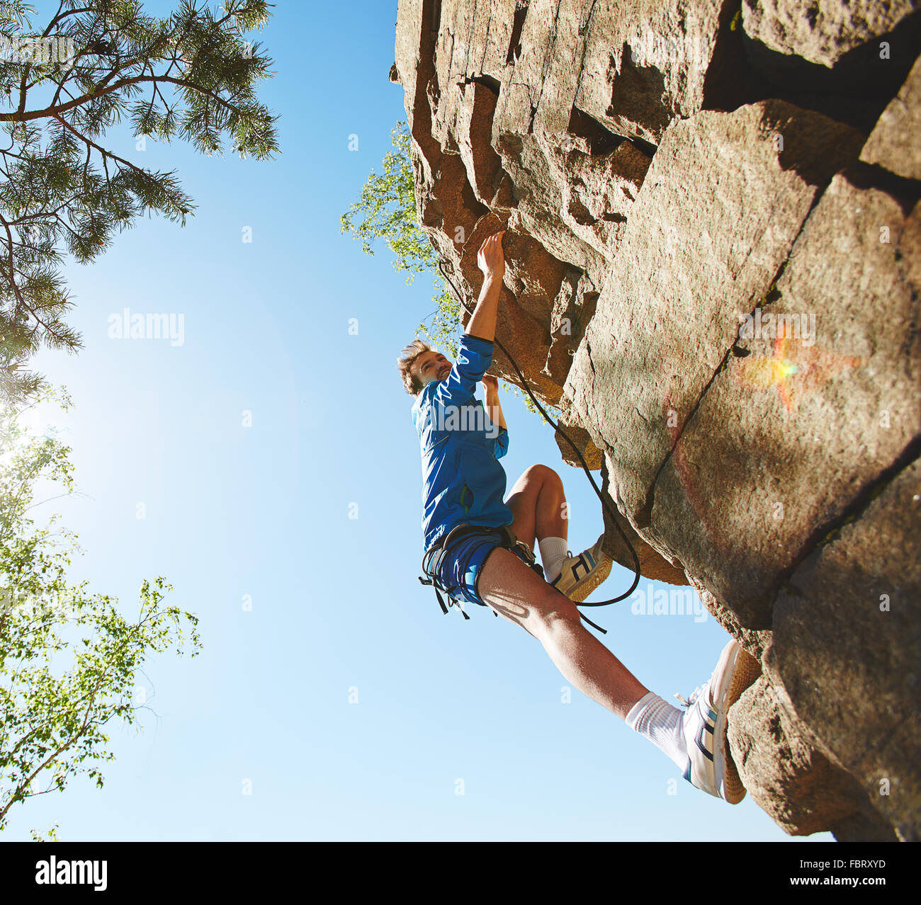 Happy young man in activewear climbing on cliff Stock Photo