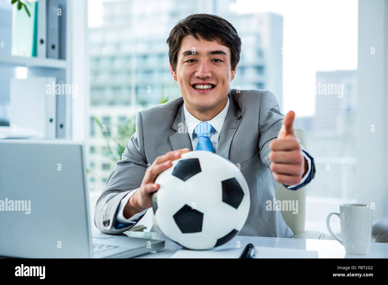Asian businessman holding soccer ball with thumps up Stock Photo