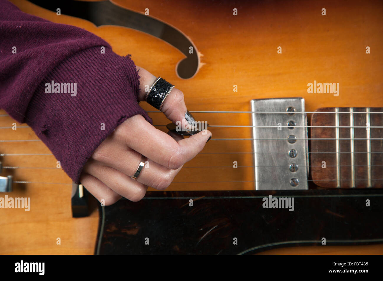 A girls hand holding a plectrum and strumming a guitar Stock Photo