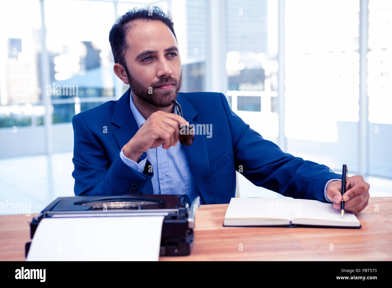 Thoughtful businessman holding pen while sitting at desk Stock Photo
