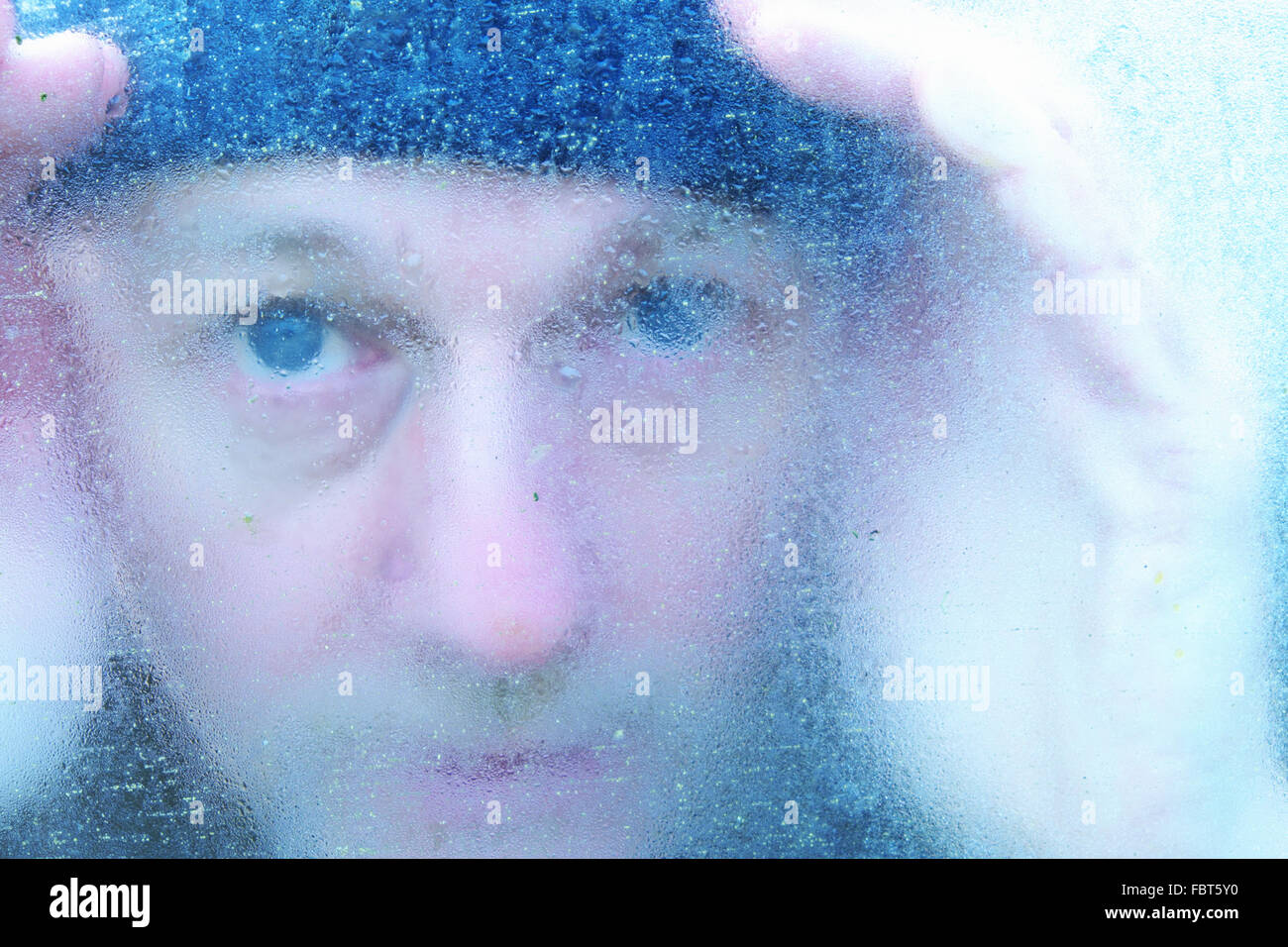 man-peering-through-a-frozen-window-pane-in-winter-FBT5Y0.jpg