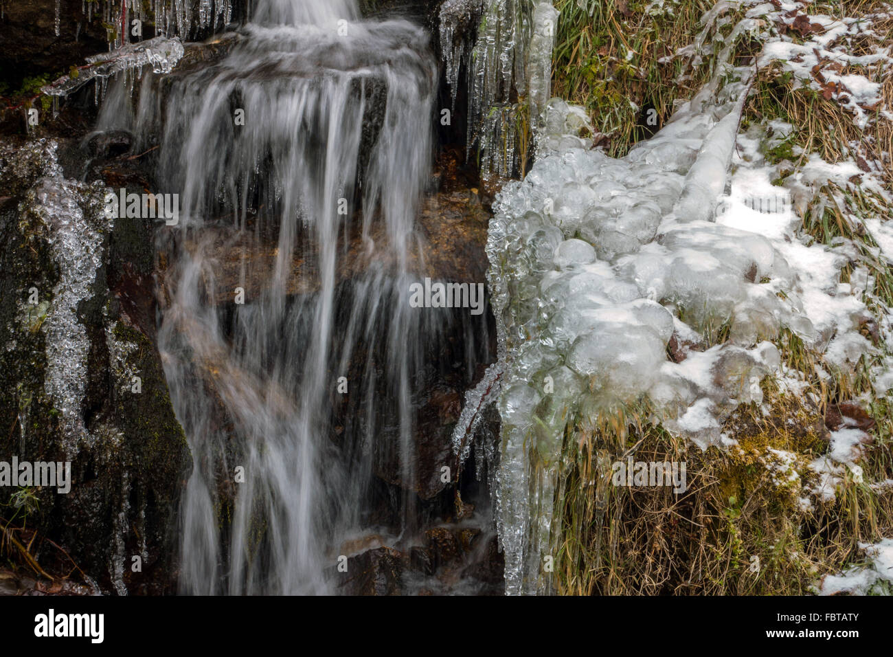 Misty running water and ice frozen onto grass in winter Stock Photo