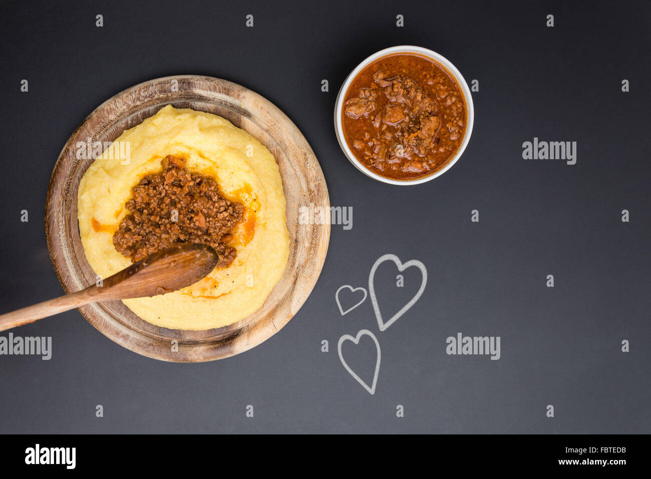 A dish of Polenta with bolognese soup (aka Ragu) standing on a black-board. Some hearts on the blackboard Stock Photo