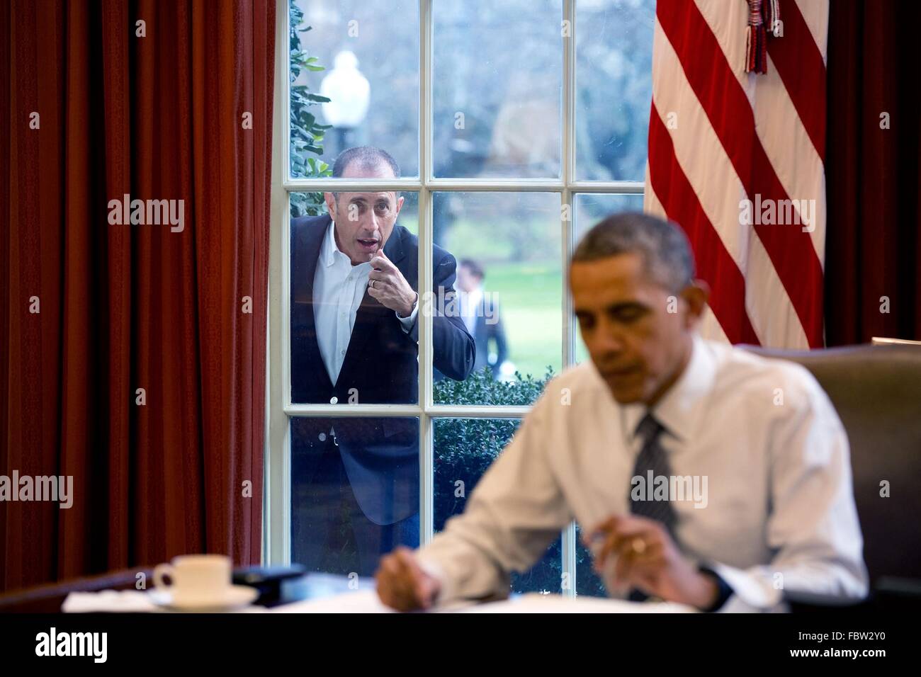 Comedian Jerry Seinfeld knocks on the Oval Office window to begin a segment for his series, Comedians in Cars Getting Coffee as U.S President Barack Obama works at the Resolute Desk December 7, 2015 in Washington, DC. Stock Photo