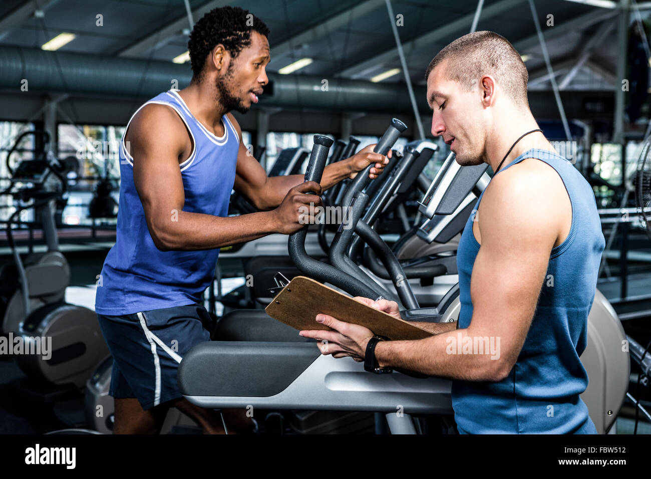 Muscular man using elliptical machine with trainer Stock Photo