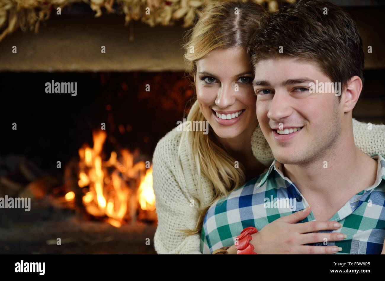 Young romantic couple sitting on sofa in front of fireplace at home