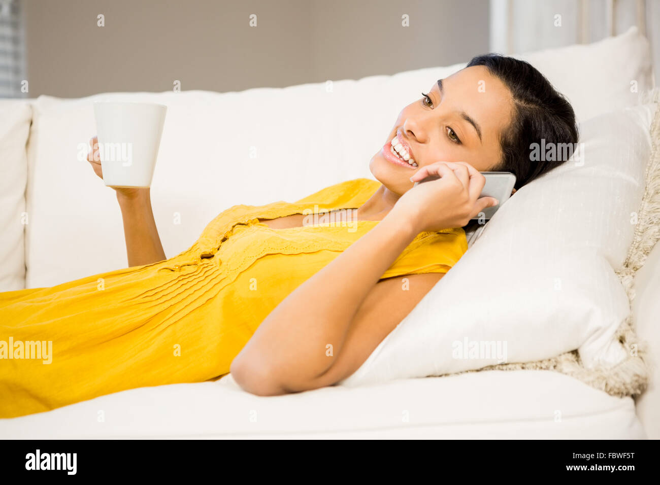 Smiling brunette on a phone call holding cup Stock Photo