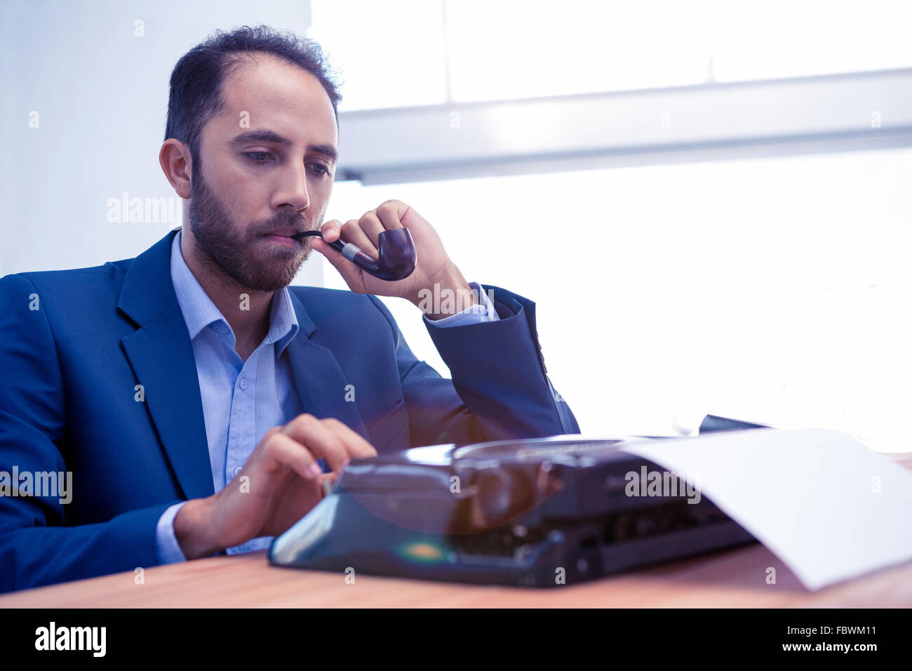 Businessman using typewriter while holding smoking pipe Stock Photo