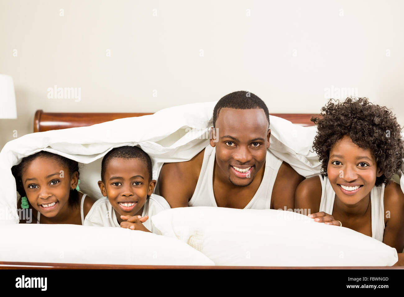 Cute family resting on bed under blanket Stock Photo