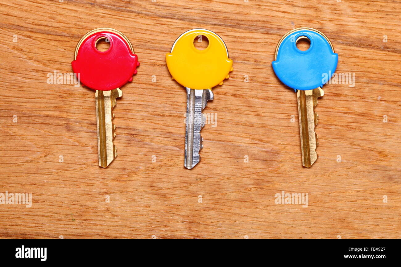 Three house keys with colorful plastic coats caps on wooden table background. Stock Photo